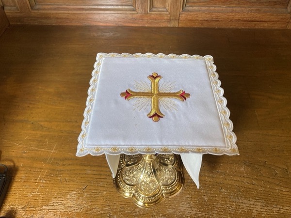 The pall – This is a small, stiff square, or rectangle made of cardboard, fabric, or other materials, often with a piece of stiffened cloth on top. It is used to cover the chalice during the celebration of the Eucharist to prevent any foreign objects or dust from coming into contact with the precious Blood.