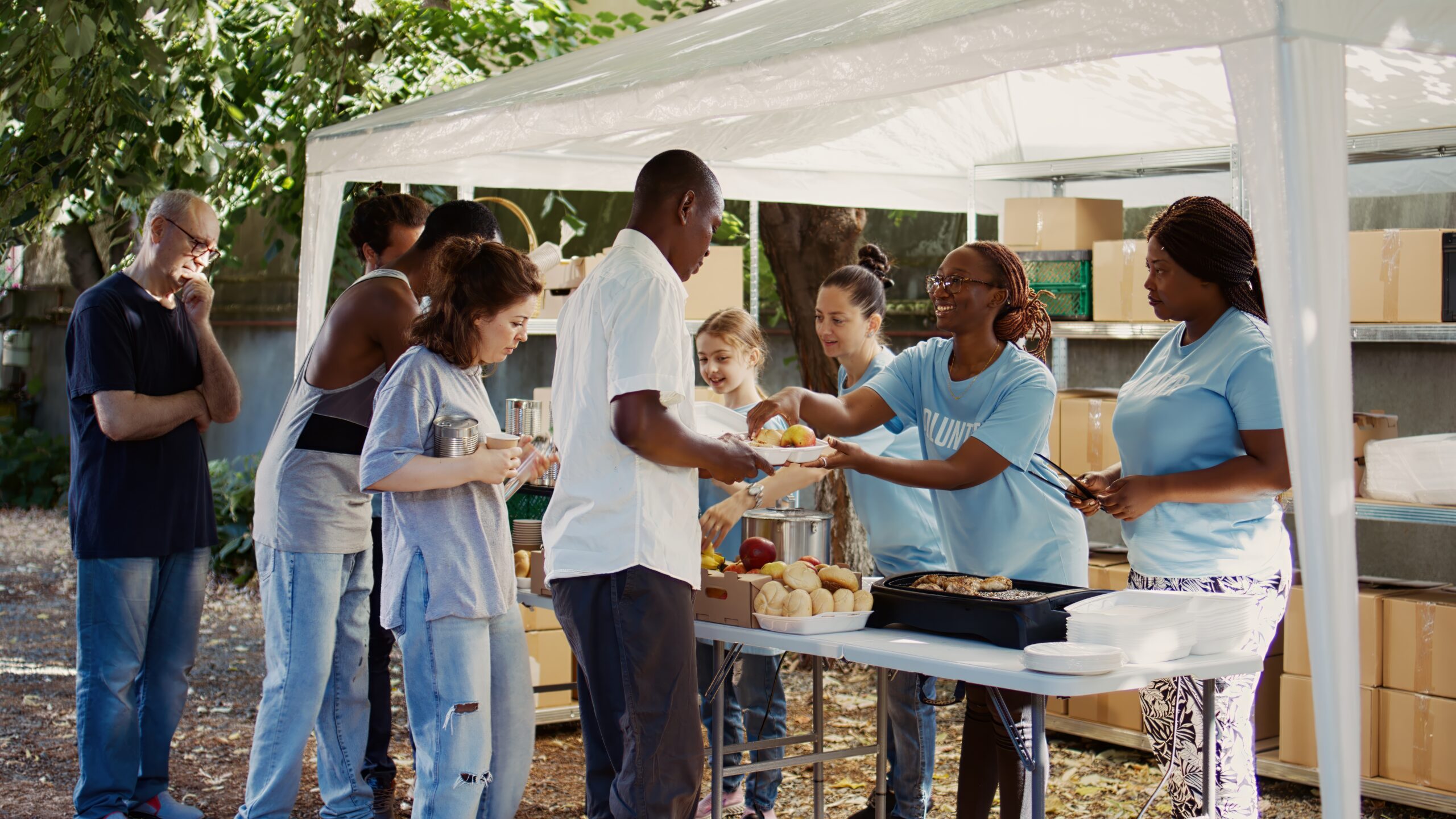 People from many backgrounds assemble outside to distribute non-perishable donations and help the poor and homeless. Multiracial volunteers provide needy individuals with free, freshly prepared meals.