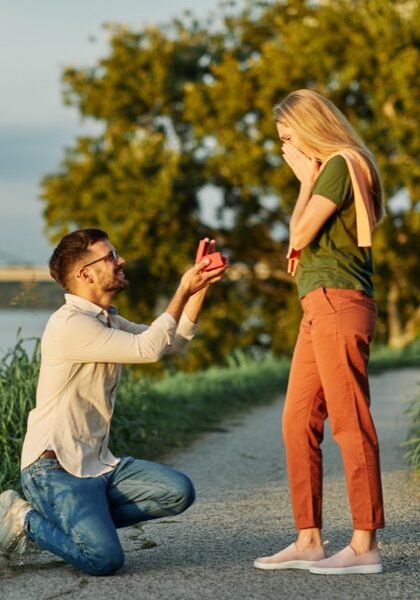 Cheerful handsome man proposing to his girlfriend. Portrait of a young happy couple having fun outdoors in nature during sunset. Girlfriend and boyfriend bonding, love concept during summer.